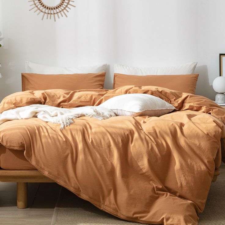 a bed with an orange comforter and pillows on it in front of a white wall