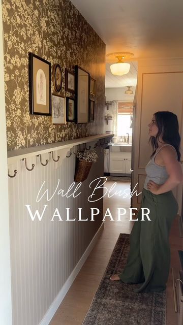 a woman standing in a hallway next to a wall with pictures on the walls and a rug