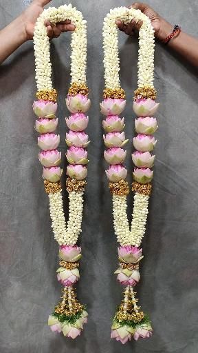 two hands are holding some white and pink flowers with gold trimmings on them