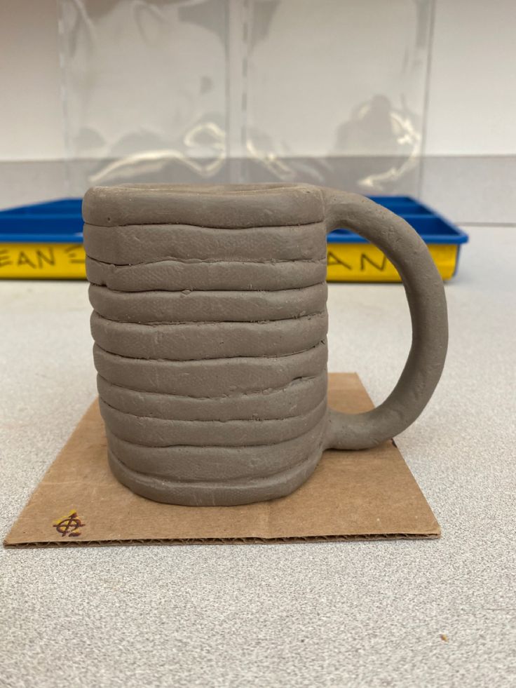 a mug made out of clay sitting on top of a piece of cardboard