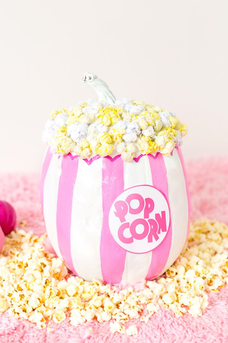 a pink and white striped popcorn bowl with pop corn in it on a pink carpet