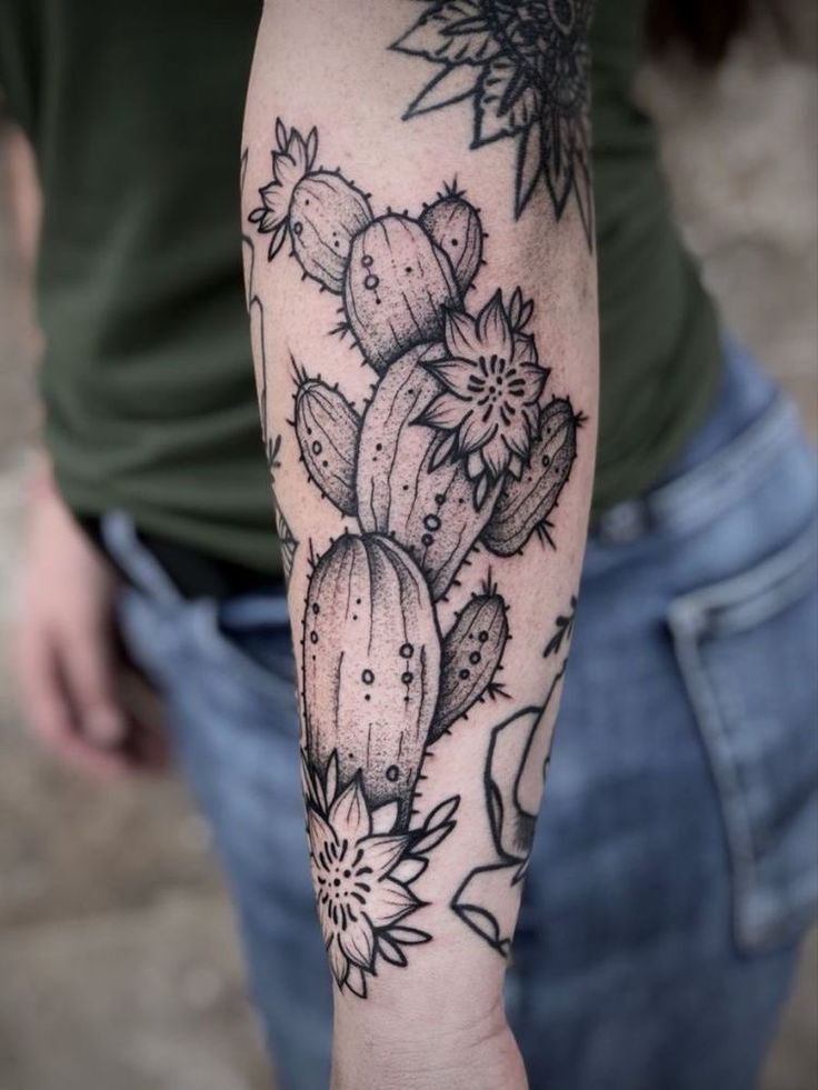 a person with a tattoo on their arm holding up a flower and cactus plant in front of them