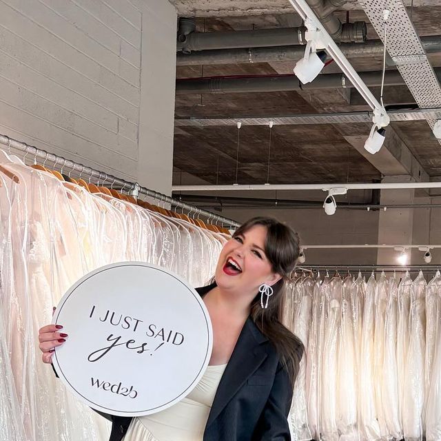 a woman holding a sign that says i just said yes in front of some dresses