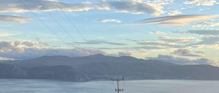 the sky is very cloudy and there are power lines in the foreground with mountains in the background