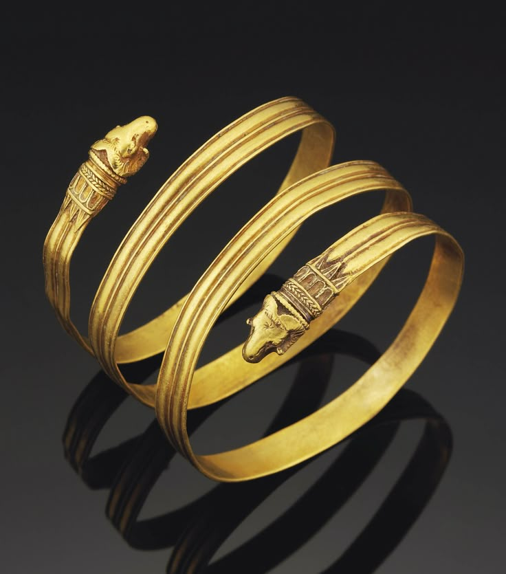 two gold bracelets with an egyptian head on each bangle, one in the shape of a snake