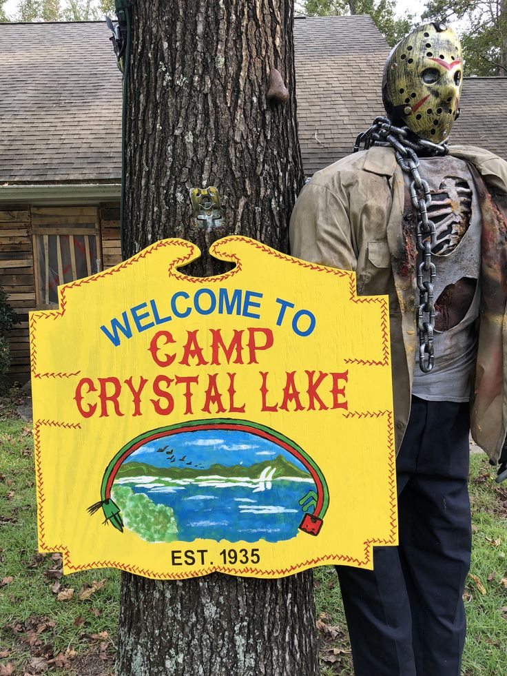 a man standing next to a tree in front of a sign that says welcome to camp crystal lake