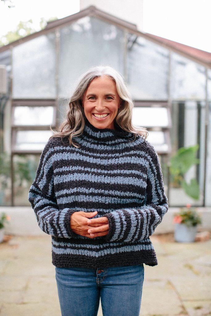 a woman standing in front of a house wearing a black and grey striped knit sweater