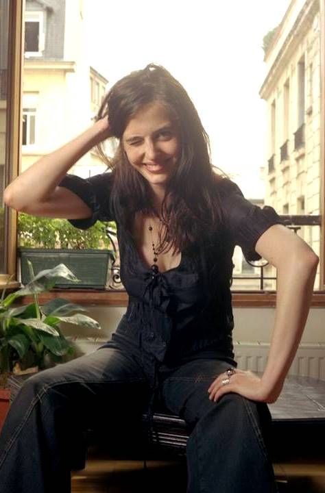 a woman sitting on top of a chair in front of a window next to a potted plant