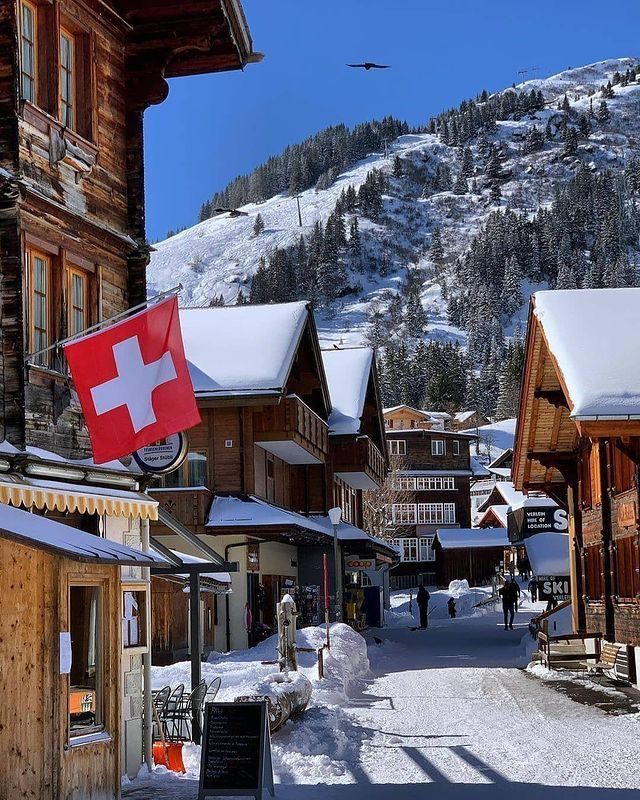 an alpine village with snow covered mountains in the background and a swiss flag flying high