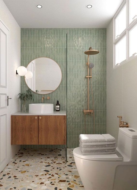 a bathroom with green tile and white fixtures, including a round mirror above the sink