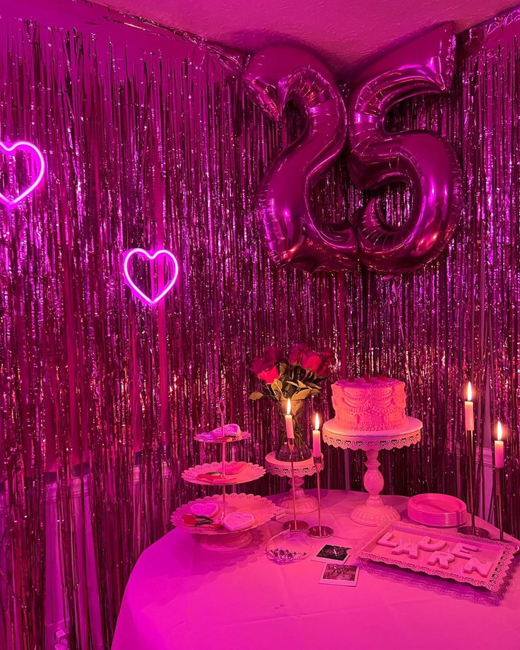 a table topped with a cake next to two candles and pink foil curtained walls