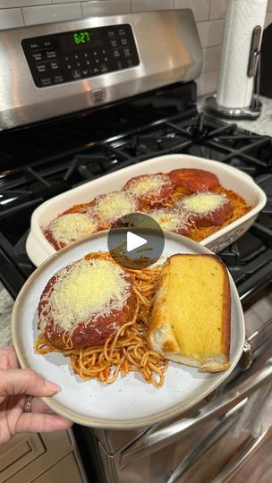 someone is holding a plate with spaghetti and bread on it in front of an oven