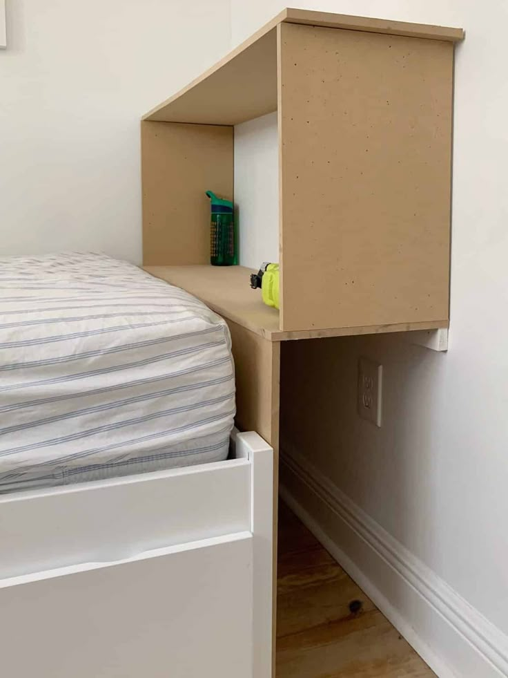 a bedroom with a bed, nightstand and small shelf next to the wall in front of it