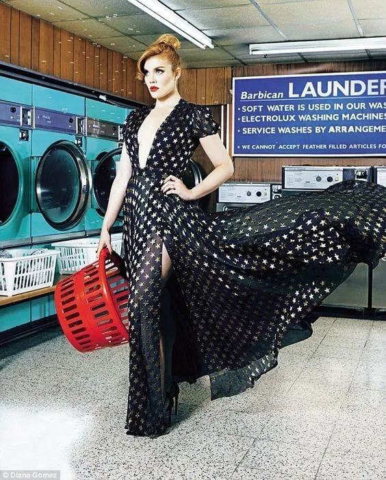 a woman in a black dress is holding a red bucket and standing next to a stack of washers