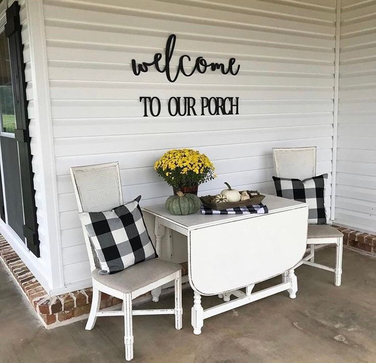 two white chairs sitting on top of a porch next to a table with flowers in it