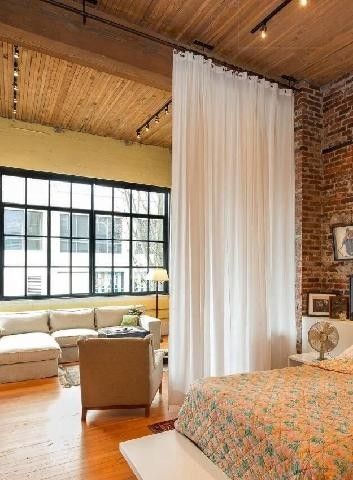 a large bedroom with brick walls and wooden flooring, along with a bed that has a floral comforter on it