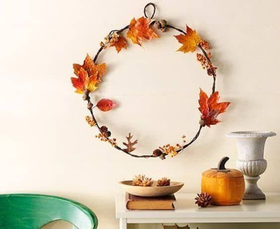 a white table topped with a green chair next to a wall mounted wreath filled with autumn leaves