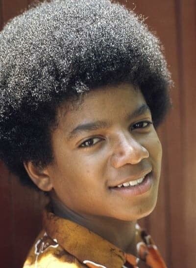 a young man with an afro smiles for the camera while standing in front of a wooden door