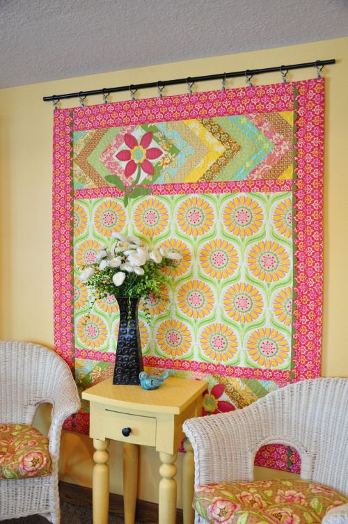 two chairs and a table in front of a wall with a colorful quilt on it