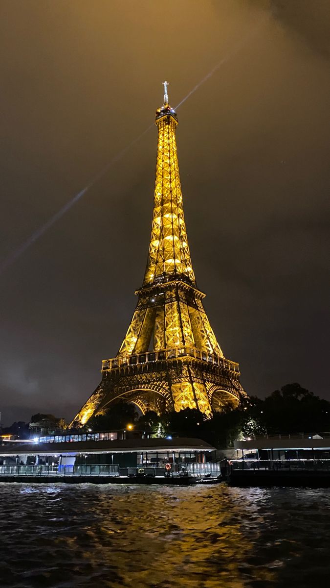 the eiffel tower lit up at night with lights reflecting off it's water