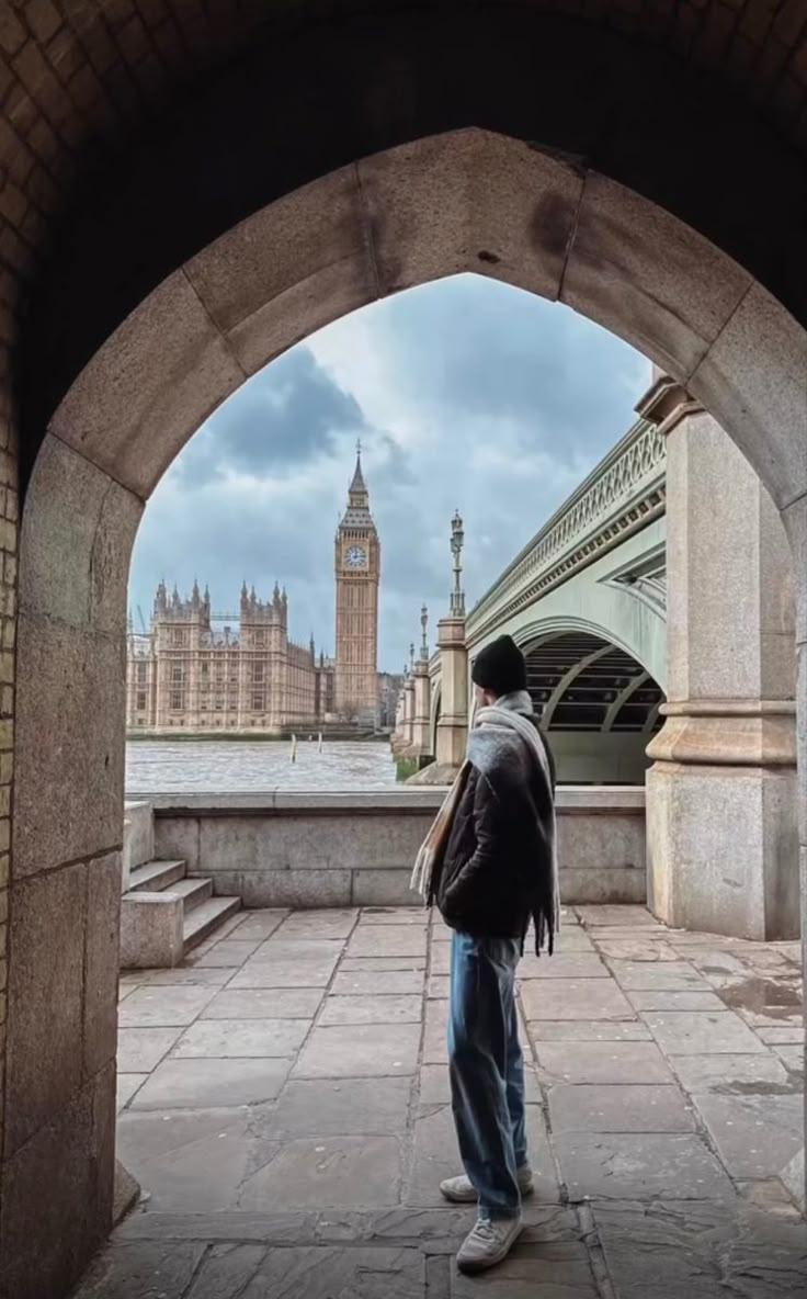 a man standing in an archway looking at the city skyline with big ben in the background