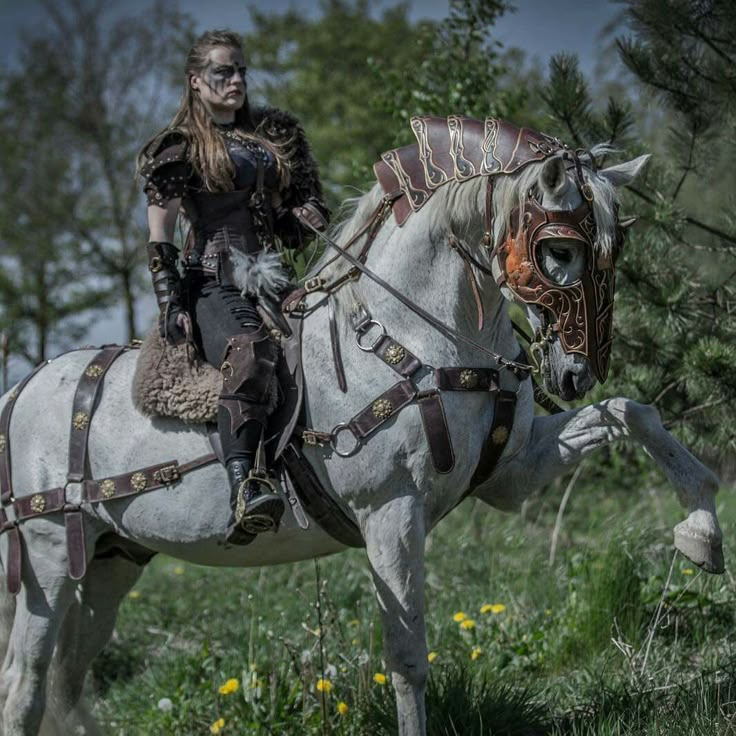 a woman riding on the back of a white horse in a field next to trees