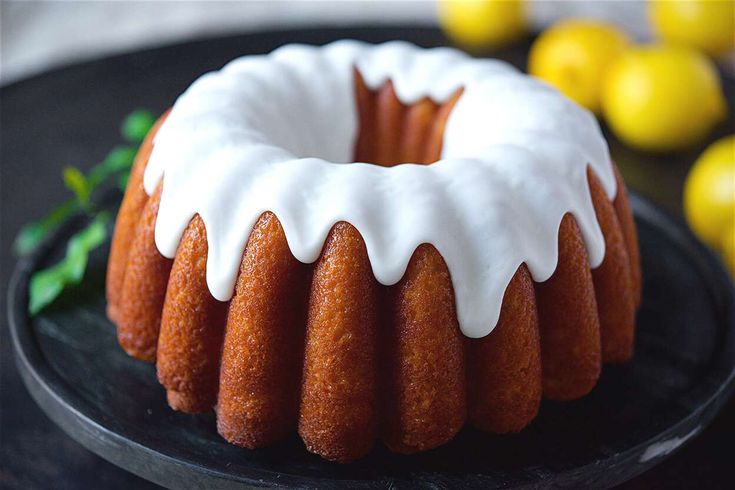 a bundt cake with white icing on a black plate next to lemons