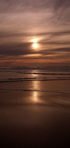 the sun is setting over the ocean with some clouds in the sky and one person walking on the beach