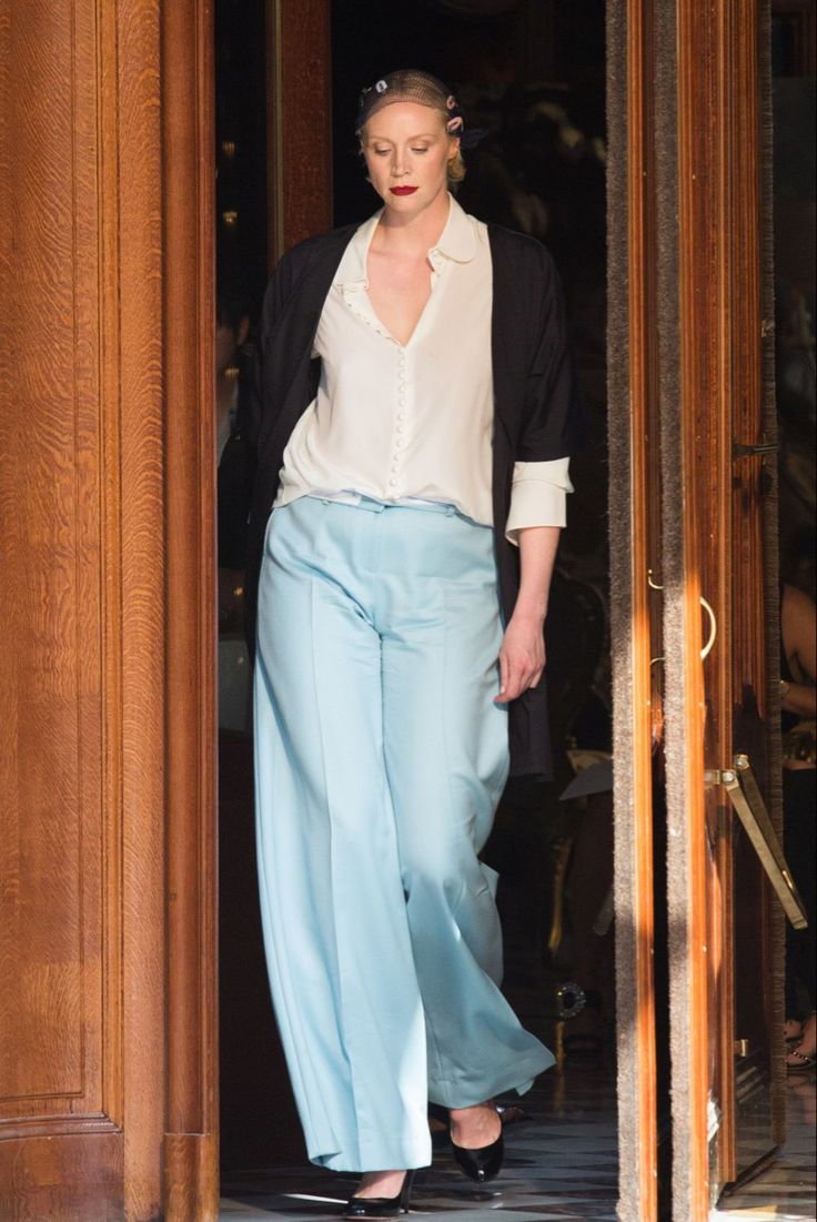 a woman in blue pants and a white shirt is walking through an open door with her hand on her hip