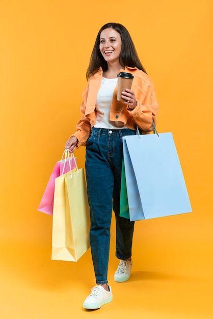 a woman is holding shopping bags and looking at her cell phone while standing against an orange background