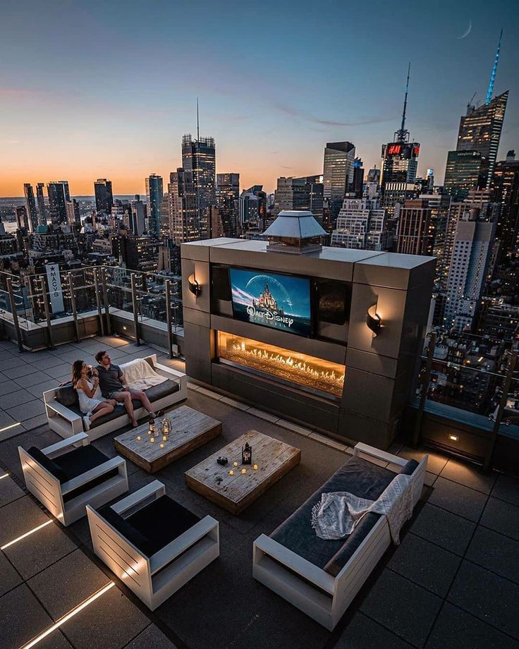 two people sitting on couches in front of a cityscape at night with the sun setting