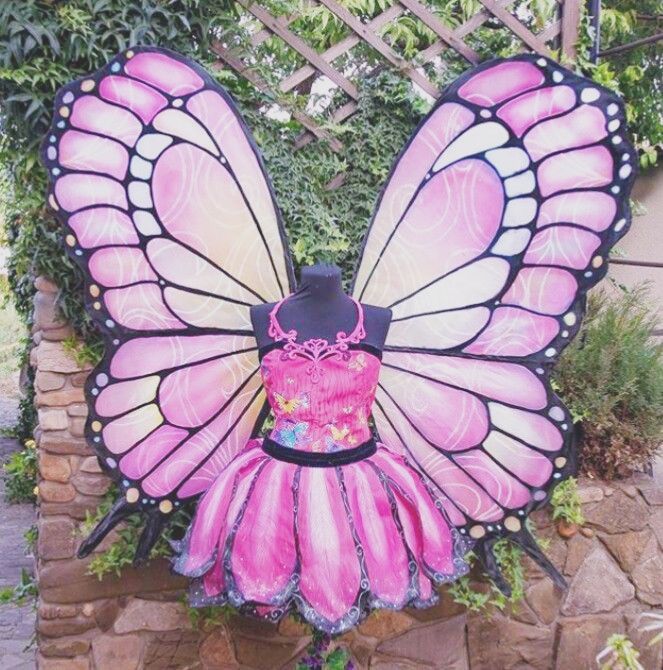 a pink and black butterfly costume sitting on top of a brick wall next to a garden