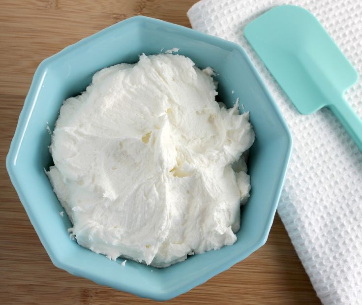 a blue bowl filled with whipped cream on top of a wooden table next to a spatula