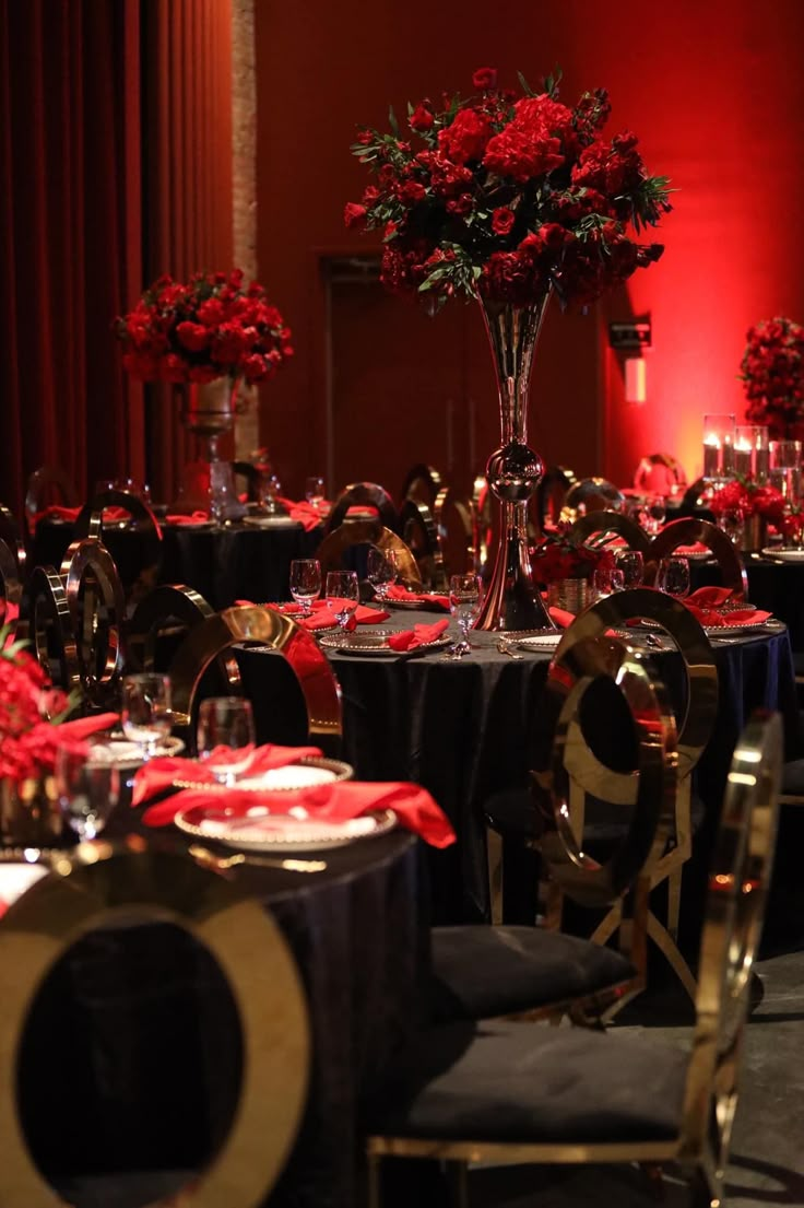 a room filled with tables covered in black and red table cloths next to tall centerpieces