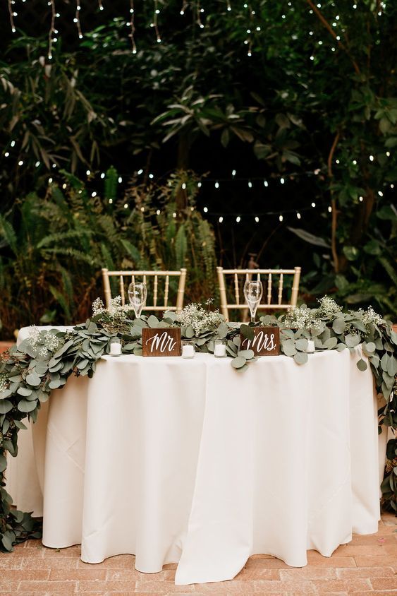 the table is set up with chairs and greenery