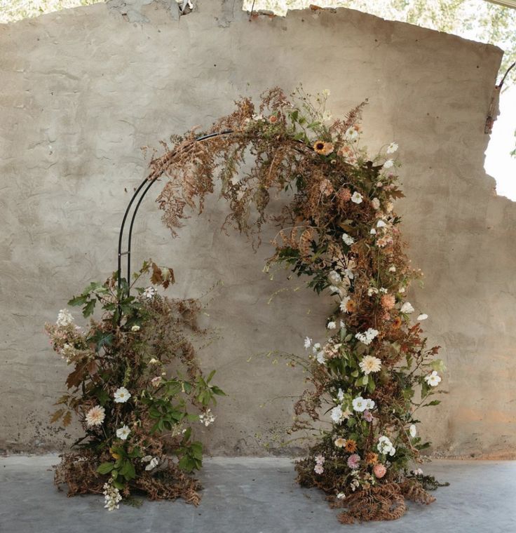 an arch made out of branches and flowers on the side of a building with concrete walls