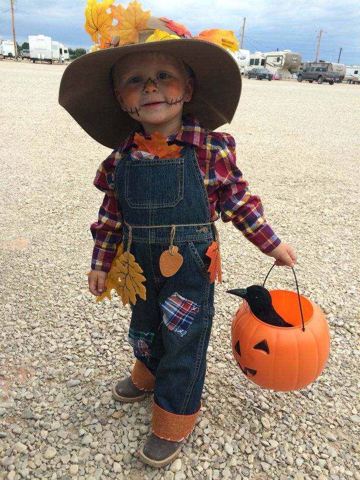 a little boy dressed up as a scarecrow holding a jack - o'- lantern