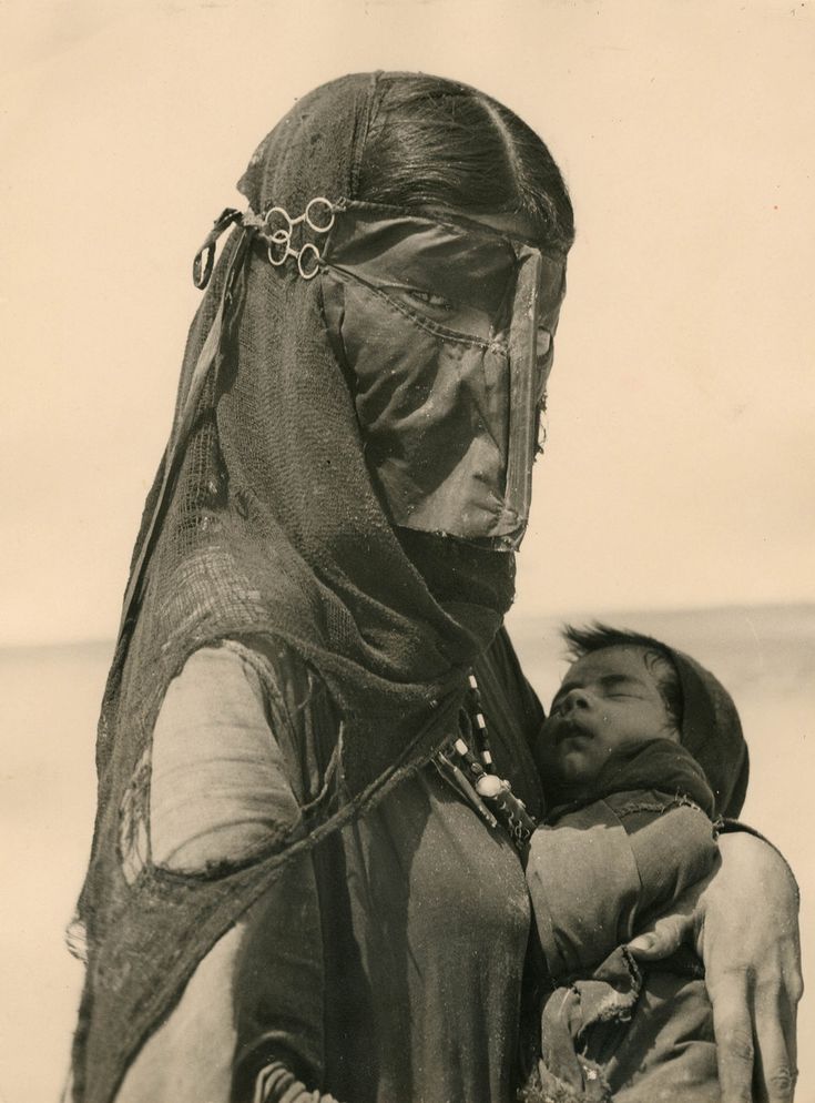 an old photo of a woman holding a baby in her arms and wearing a headdress