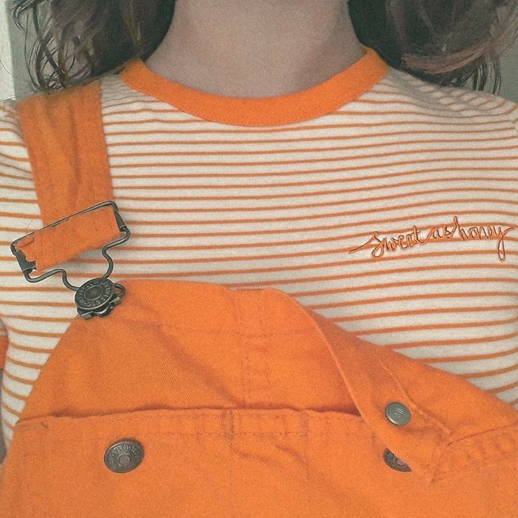 a woman wearing an orange bib and suspenders with her hands in her pockets