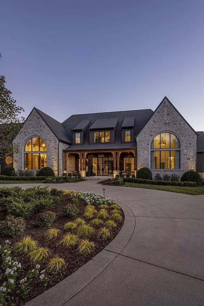 a large house with lots of windows in the front yard and landscaping around it at night