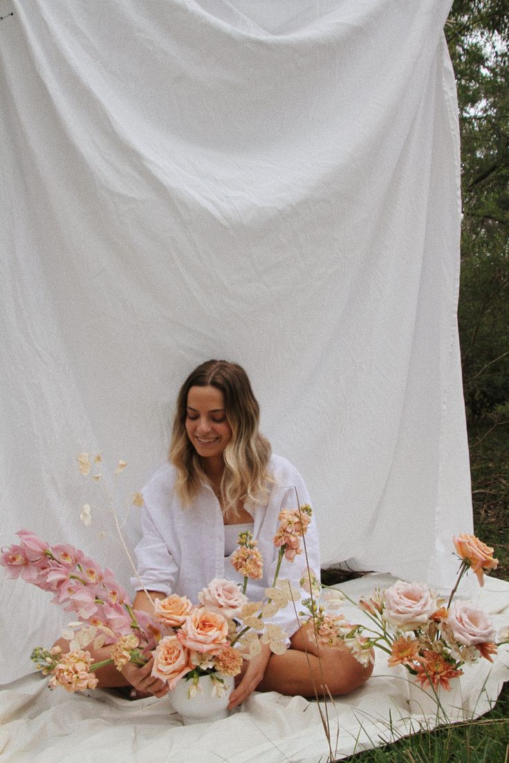 a woman sitting on the ground with flowers in front of her