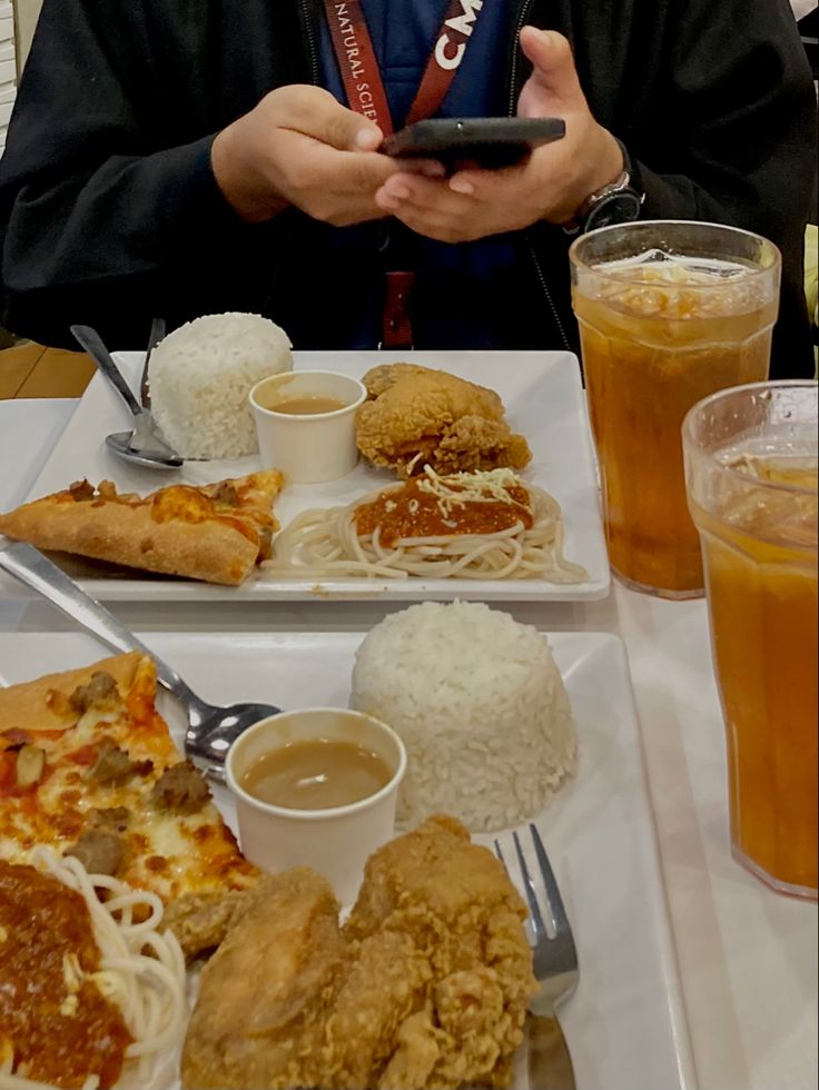 a man sitting at a table with food and drinks in front of him while looking at his cell phone