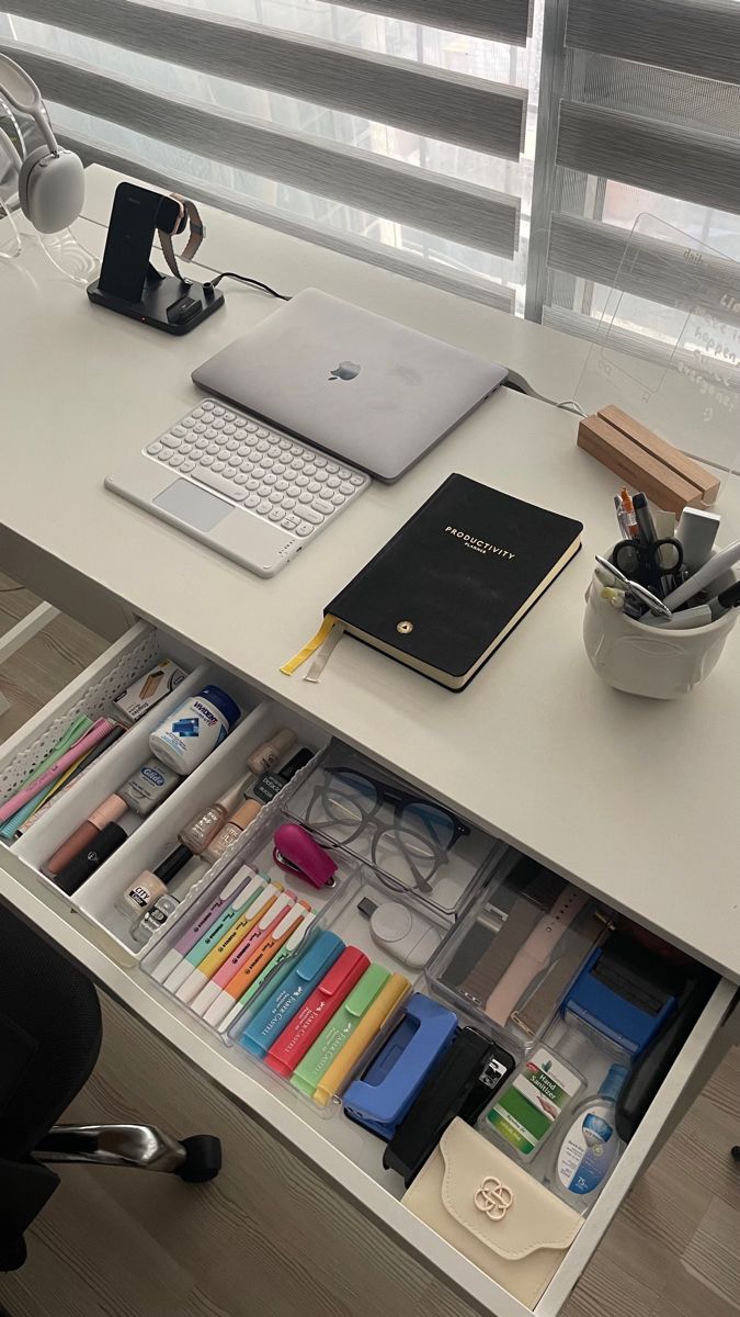 an office desk with a laptop, books and other items on it in front of a window