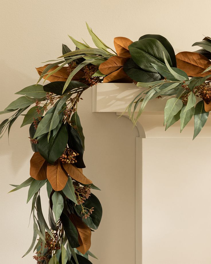 a wreath with leaves and berries hanging from the mantle in front of a white wall