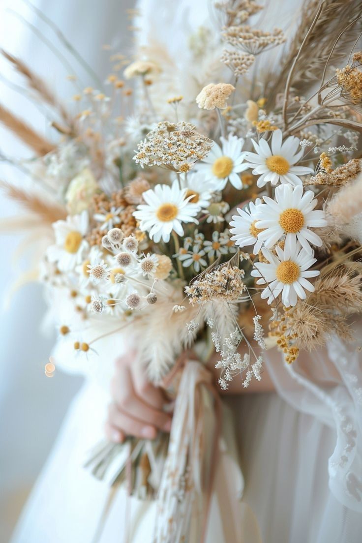 a bride holding a bouquet of daisies and feathers