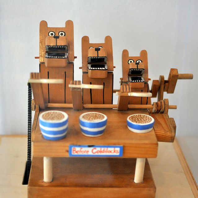 three wooden cats sitting on top of a table with bowls and cups in front of them