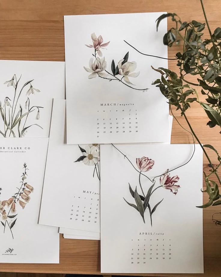 four calendars with flowers on them sitting on top of a wooden table next to a potted plant