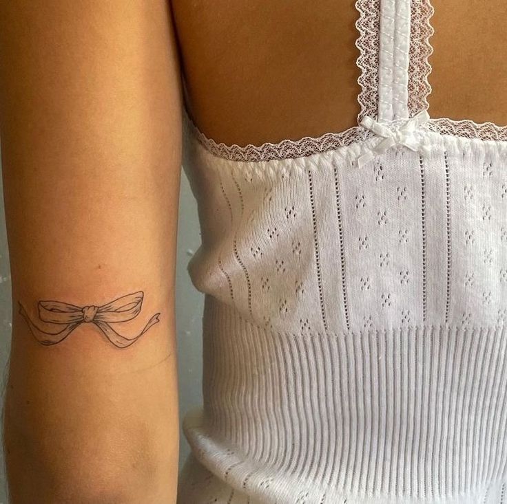 a woman's arm with a bow tattoo on the left side of her arm