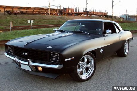 a black muscle car is parked on the side of the road in front of some train tracks