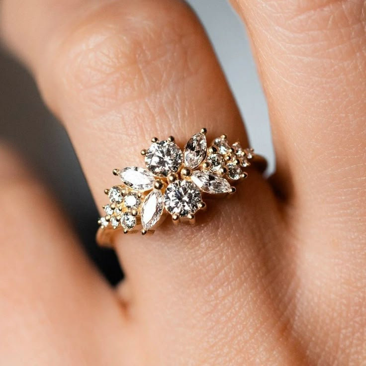 a woman's hand wearing a gold ring with white stones on it and leaves